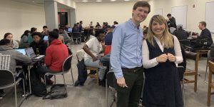 Students gathered in a meeting room, grouped at different tables. Professors Hernisa Kacorri and David Weintrop are standing in the foreground, smiling at the camera.