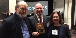 Dr. Gregg Vanderheiden, Dr. Jonathan Lazar, and Dr. Susan Winter (left to right) standing inside the conference venue at the 2020 UMD Research Excellence Celebration. Dr. Lazar is holding an award plaque.